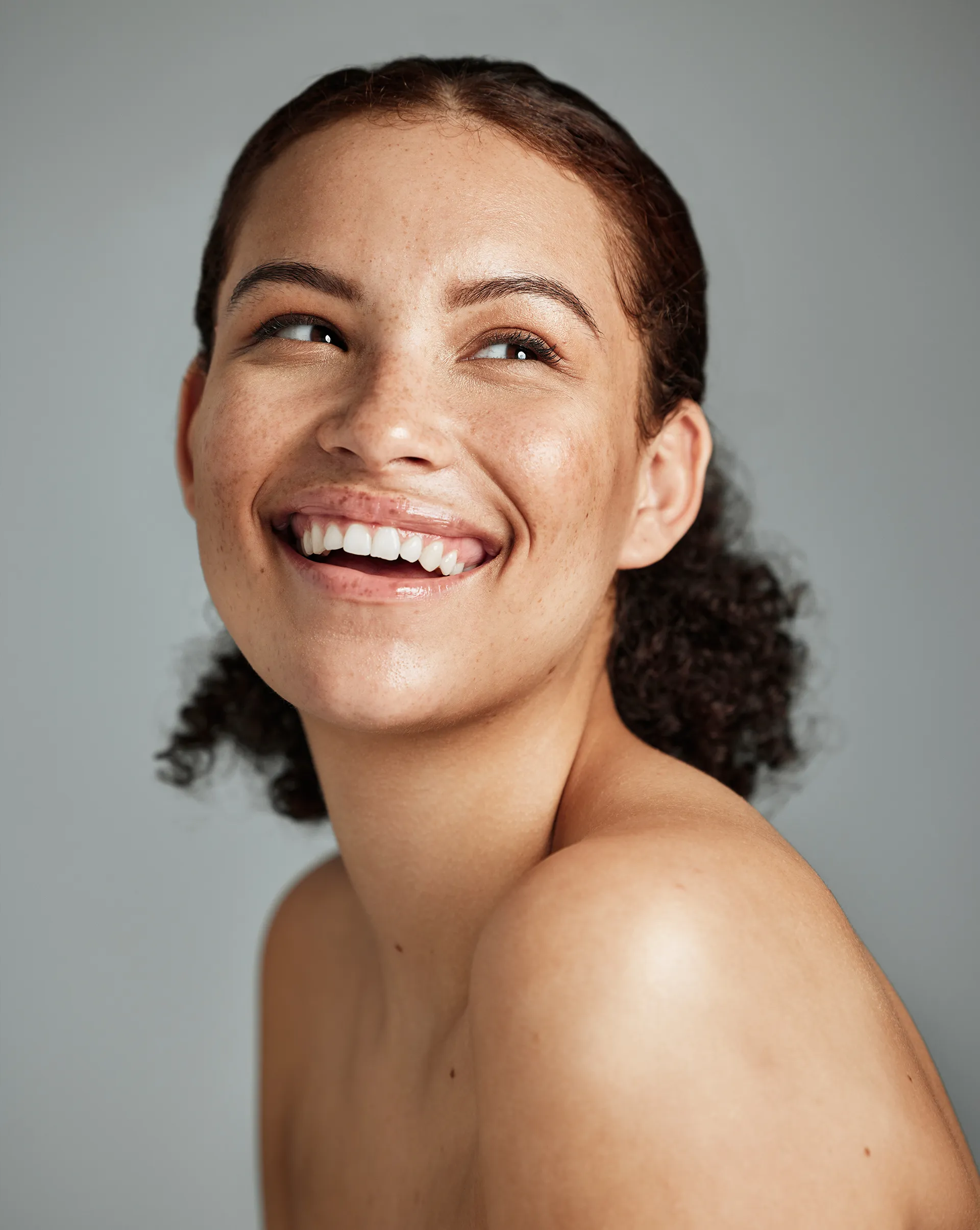 Smiling woman with clear skin looking upwards against a neutral background