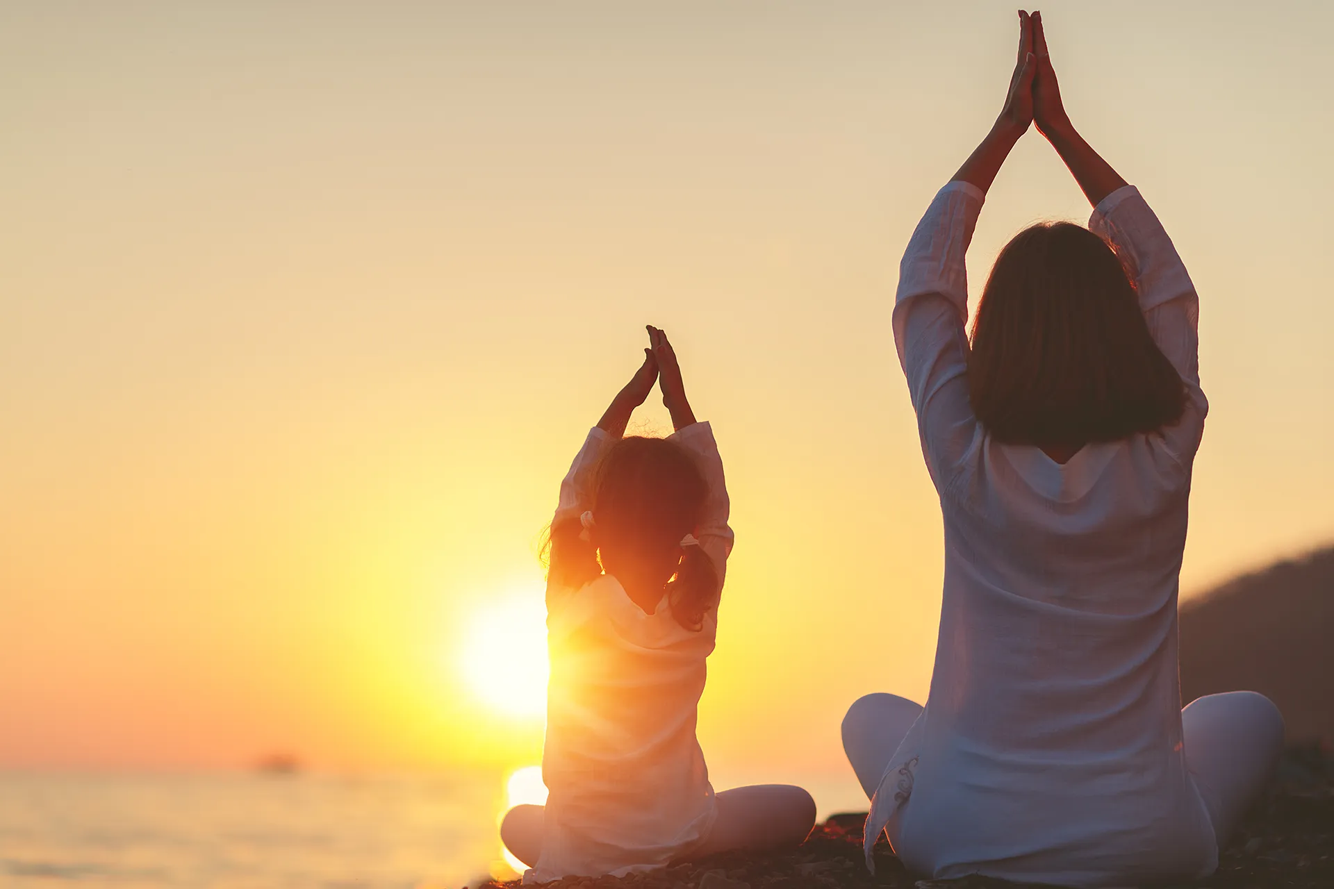 Mother and daughter practicing yoga at sunrise by the sea.