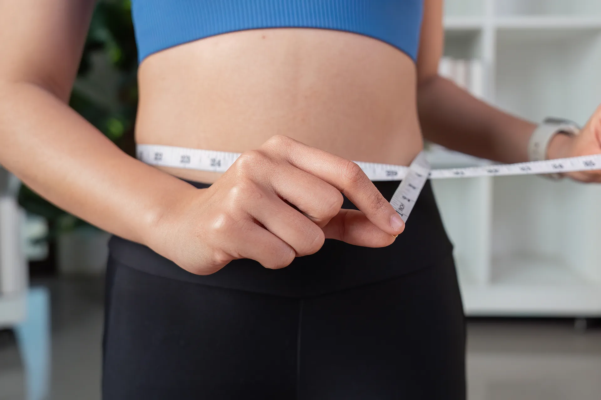 Person measuring waist with tape in fitness setting.