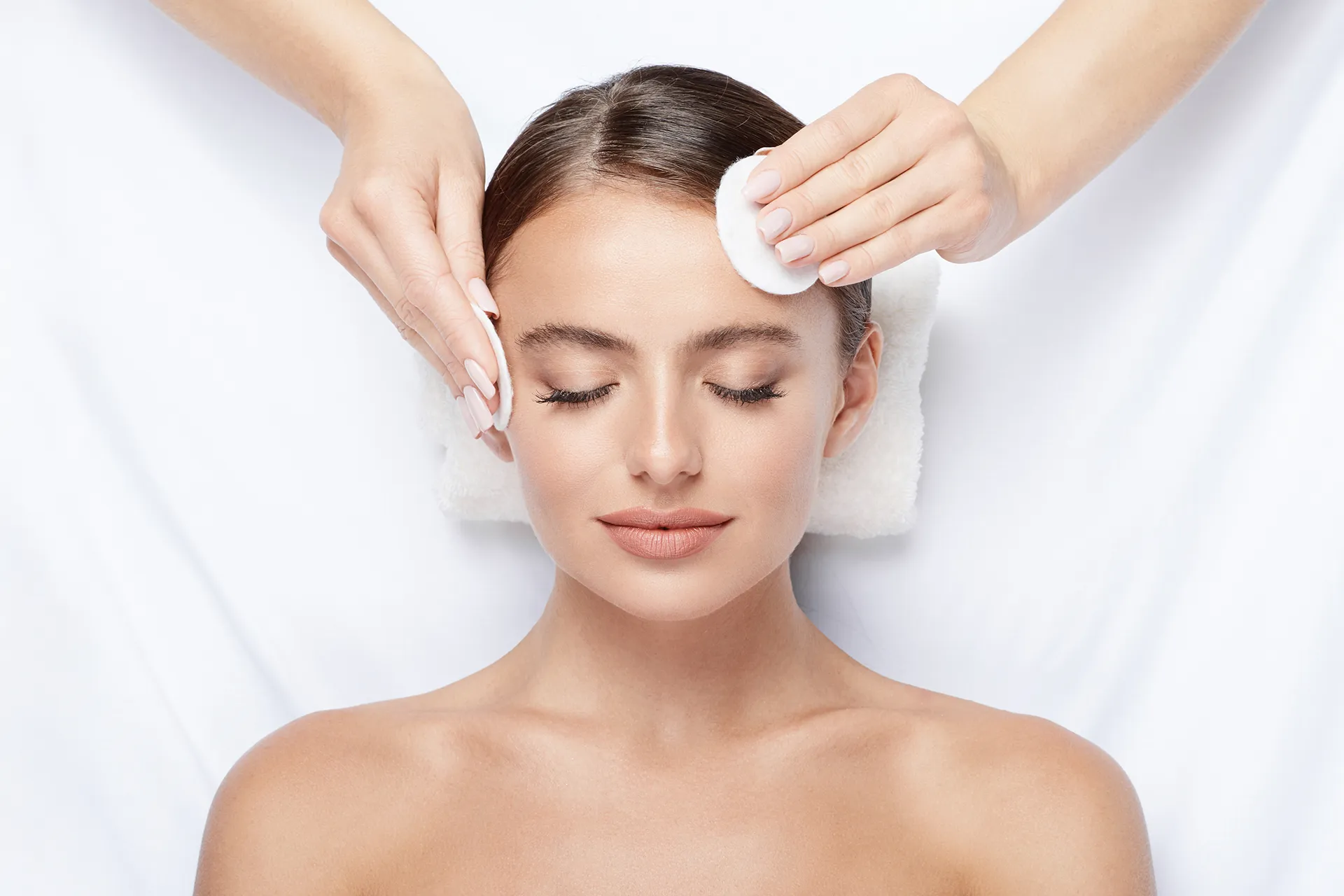 Woman receiving a facial treatment with cotton pads at a spa.