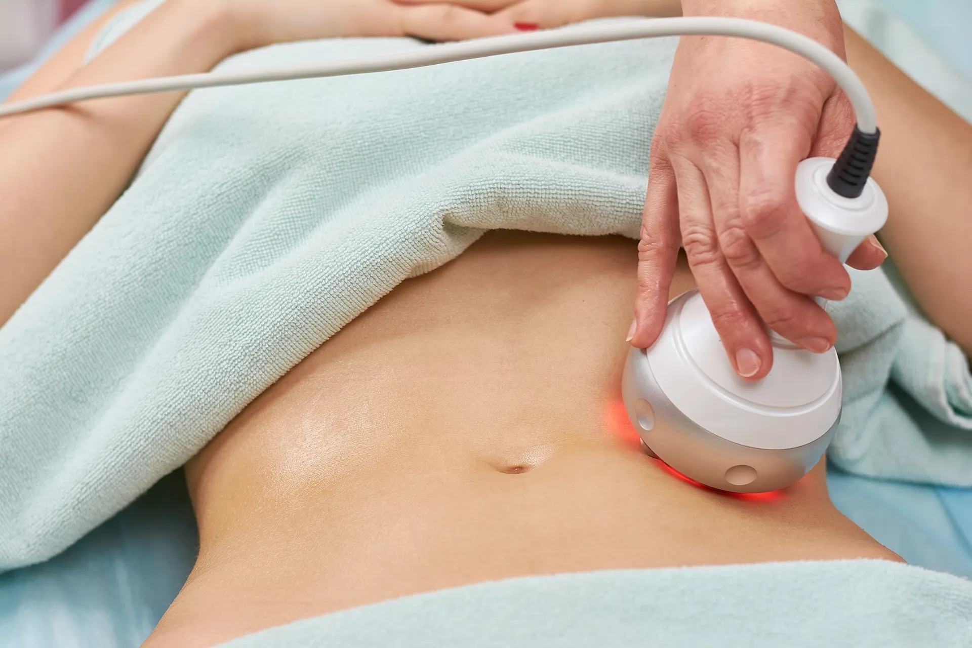 A close-up of a handheld beauty treatment device being used on a person's abdomen, with red light emanating from the device.
