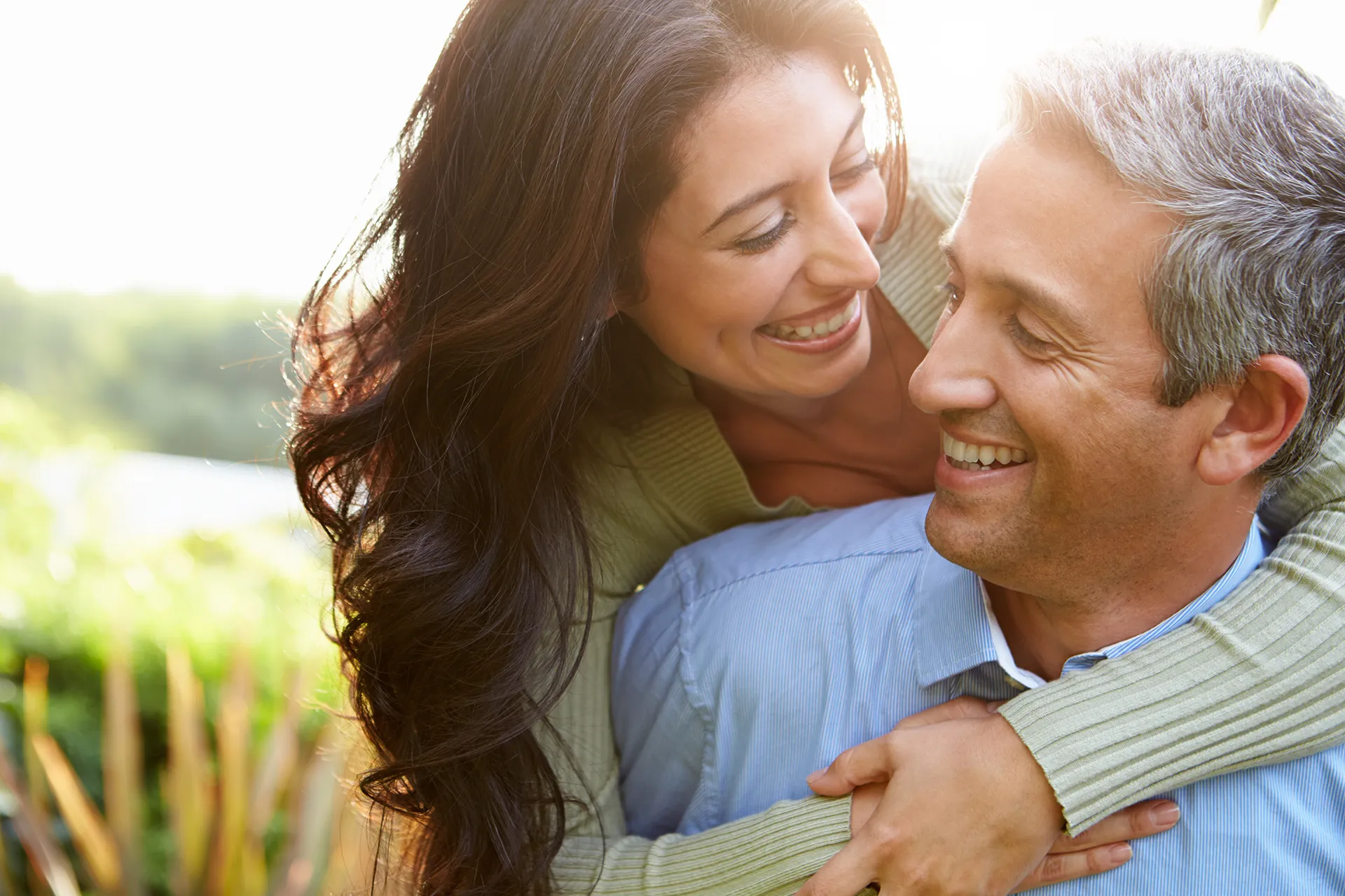 Couple laughing and having a joyful moment outdoors, with the woman playfully hugging the man from behind.