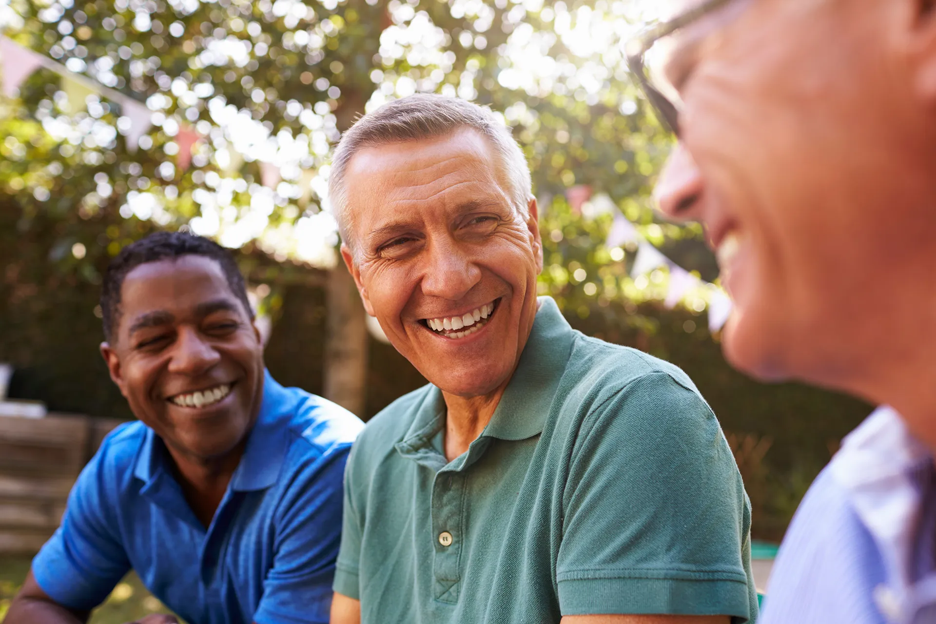 Three men smiling and enjoying a relaxed moment outdoors, surrounded by greenery.