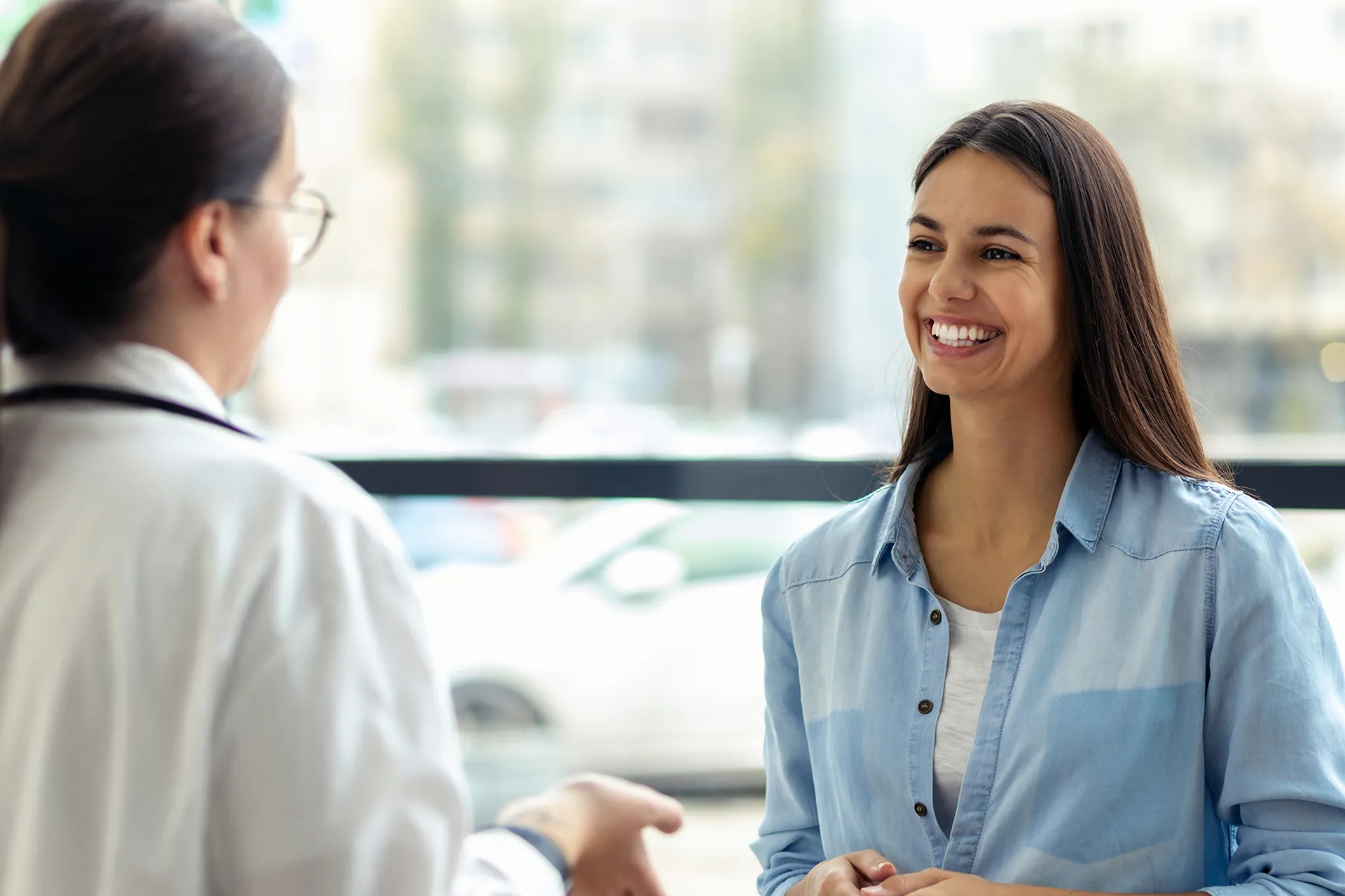 A smiling young woman conversing with a doctor in a medical office.