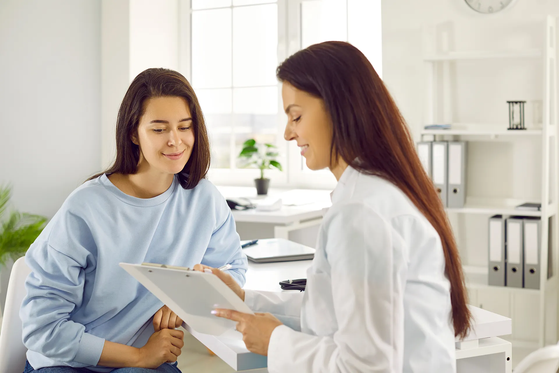 Young woman sitting across from a doctor during a medical consultation at an office.