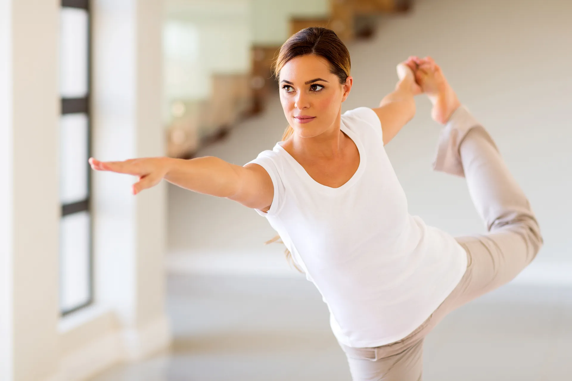 Woman practicing yoga and balancing on one leg in a bright indoor space