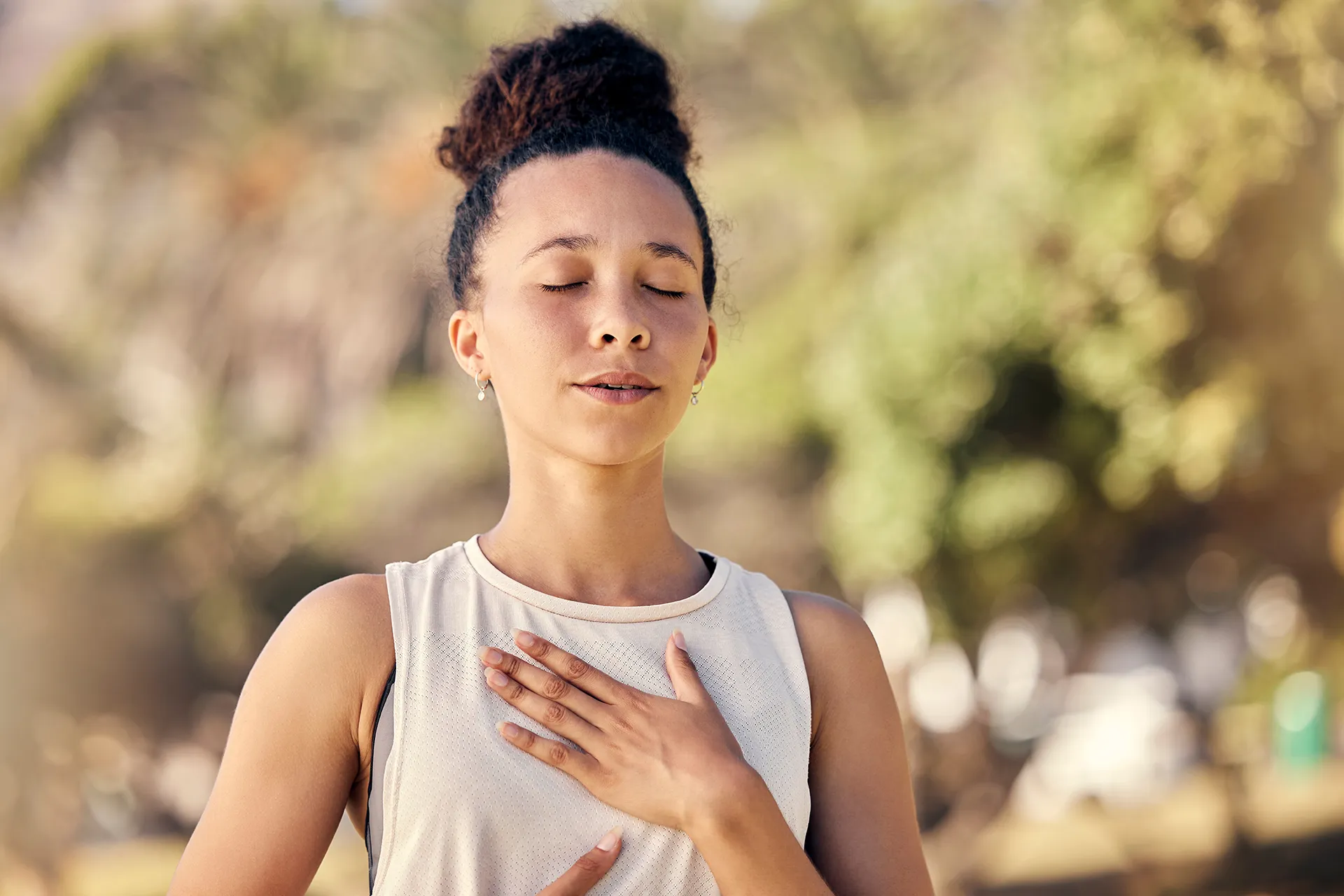 A young woman practicing mindfulness outdoors, with her eyes closed and a serene expression.